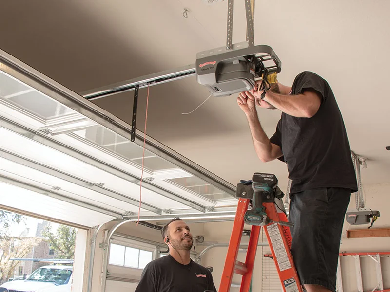 Two Titletown Garage Door technicians servicing a LiftMaster belt-drive opener from a ladder in a Green Bay residential garage